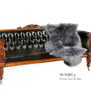 May include: A gray faux fur rug is placed on a black leather sofa with wooden arms and legs. The rug is soft and fluffy, and it adds a touch of warmth and luxury to the room. The text "FUR ACCENTS® Premium Faux Fur Rugs" is visible in the bottom right corner of the image.