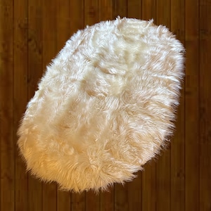 May include: A white fluffy round rug with a soft, plush texture. The rug is made of faux fur and is perfect for adding a touch of warmth and comfort to any room.