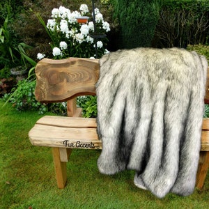 Puede incluir: Una manta de piel sintética negra y blanca drapeada sobre un banco de madera en un jardín. La manta está hecha por Fur Accents.
