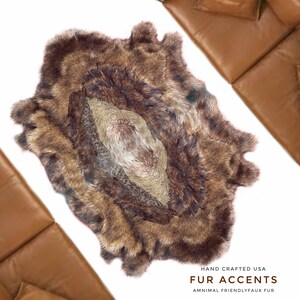 May include: A faux fur rug with a brown and tan animal print pattern. The rug has an irregular shape and is made of soft, plush material. The words "FUR ACCENTS" and "ANMIMAL FRIENDLYFAUX FUR" are printed on the image.