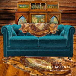 May include: A teal blue velvet sofa with a brown faux fur throw pillow and a brown faux fur rug on the floor. The rug has the text "FUR ACCENTS" and "ANIMAL FRIENDLY FAUX FUR" printed on it. The text "HAND CRAFTED USA" is also printed on the rug.