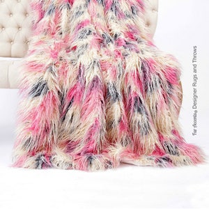 May include: A fluffy pink, white, and gray faux fur throw blanket draped over a white tufted sofa. The blanket has a soft, shaggy texture and is perfect for adding warmth and comfort to any room.