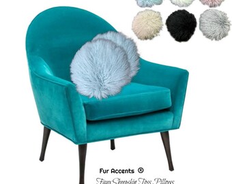 May include: A teal velvet armchair with dark wooden legs, holding two light blue faux sheepskin toss pillows. Additional round pillows in various colors are displayed above. The text "Fur Accents" and "Faux Sheepskin Toss Pillows" are visible.