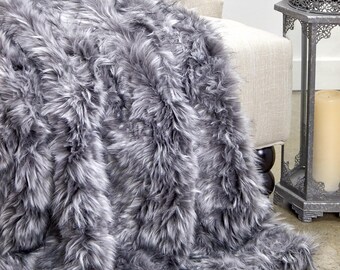 May include: A soft, grey faux fur throw blanket draped over a chair. The blanket has a long, shaggy pile and is made of a luxurious, plush material.