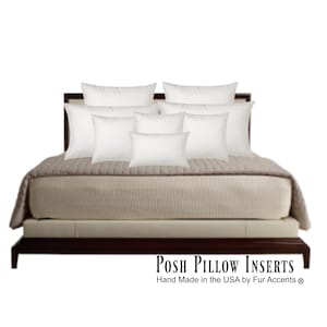May include: A bed with a dark brown frame and a beige mattress is topped with a beige quilted blanket and several white pillows of various sizes. The text "Posh Pillow Inserts" is displayed at the bottom.