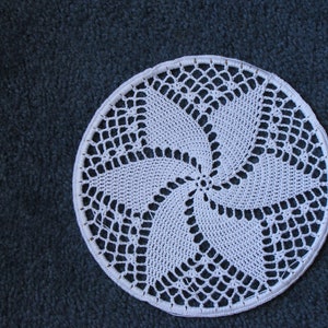 May include: White crocheted doily with a spiral design. The doily is circular and has a delicate lace pattern.