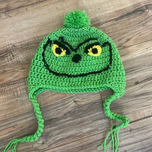 May include: Green crocheted hat with a Grinch face and a green pom pom on top. The hat has long green ties.