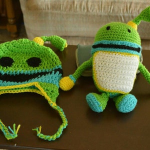 May include: A green and yellow crocheted hat with a black and blue stripe and a green and yellow crocheted robot toy.