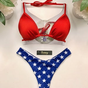 May include: Red bikini top with a triangle shape and a white star print bikini bottom. The bikini bottom has a high cut leg and a low rise. The bikini is labeled "Bonny Bikini".
