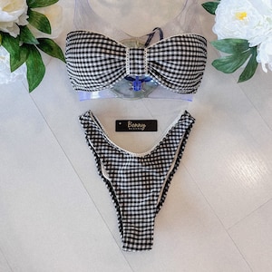 May include: Black and white gingham bikini top and bottom with a bow detail on the top. The bikini is on a white surface with a tag that says "Bonny Bikini".