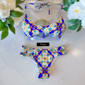 Puede incluir: Bikini estampado azul y blanco con top halter y parte inferior de cintura alta. El bikini tiene un diseño geométrico con detalles dorados. La etiqueta del bikini dice "Bonny Bikini".