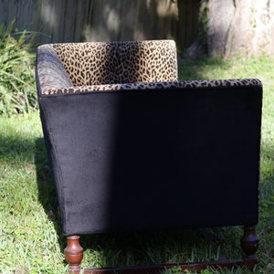 May include: A black and brown patterned sofa with wooden legs. The sofa is upholstered in a leopard print fabric.