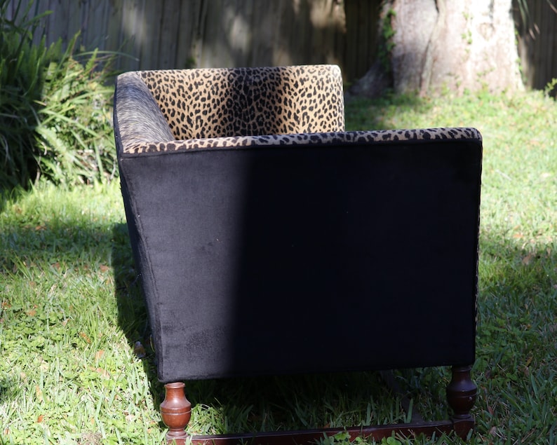 May include: A black and brown patterned sofa with wooden legs. The sofa is upholstered in a leopard print fabric.