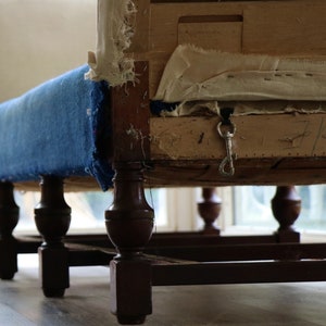 May include: A blue upholstered chair with wooden legs and a metal hook attached to the underside of the seat. The chair is in need of repair, with the upholstery showing signs of wear and tear.