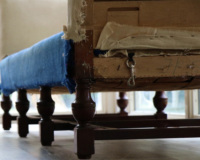 May include: A blue upholstered chair with wooden legs and a metal hook attached to the underside of the seat. The chair is in need of repair, with the upholstery showing signs of wear and tear.