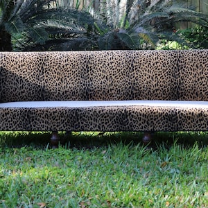 May include: A long, brown and black leopard print sofa with wooden legs. The sofa is sitting on a green grassy lawn.