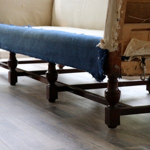 May include: A vintage sofa with a blue fabric cushion and wooden legs. The sofa is in need of reupholstery, as the fabric is torn and the cushion is sagging.