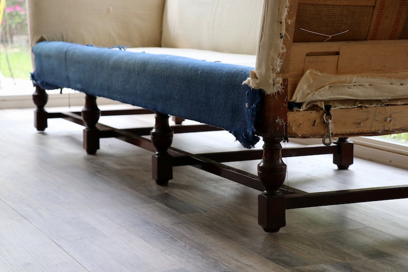 May include: A vintage sofa with a blue fabric cushion and wooden legs. The sofa is in need of reupholstery, as the fabric is torn and the cushion is sagging.