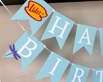 May include: A light blue swallowtail banner featuring white letters spelling out part of a message. One flag displays a yellow and red logo with the text Luke's, while another flag features a purple dragonfly graphic next to the letter B.
