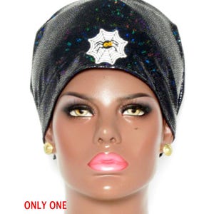 May include: A black beanie with a subtle iridescent shimmer and a white spiderweb patch featuring a small spider with yellow eyes. The text on the image reads ONLY ONE, Euro Style, Fabric #S639, and Spider. The beanie has a fitted, rounded shape.