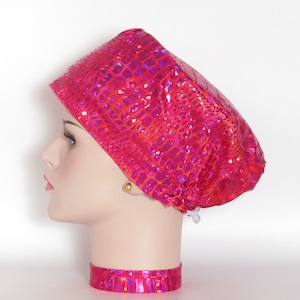 May include: A pink surgical scrub hat with a crocodile skin pattern. The hat has a drawstring closure and is made of a shiny, iridescent fabric.