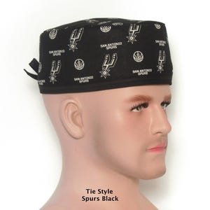 Puede incluir: Gorra negra estilo corbata con un patr&oacute;n blanco repetido del logotipo de los San Antonio Spurs. La gorra la lleva un maniqu&iacute;. El texto "SAN ANTONIO SPURS" tambi&eacute;n est&aacute; impreso en la gorra. El texto "Tie Style Spurs Black" est&aacute; impreso en la parte inferior.