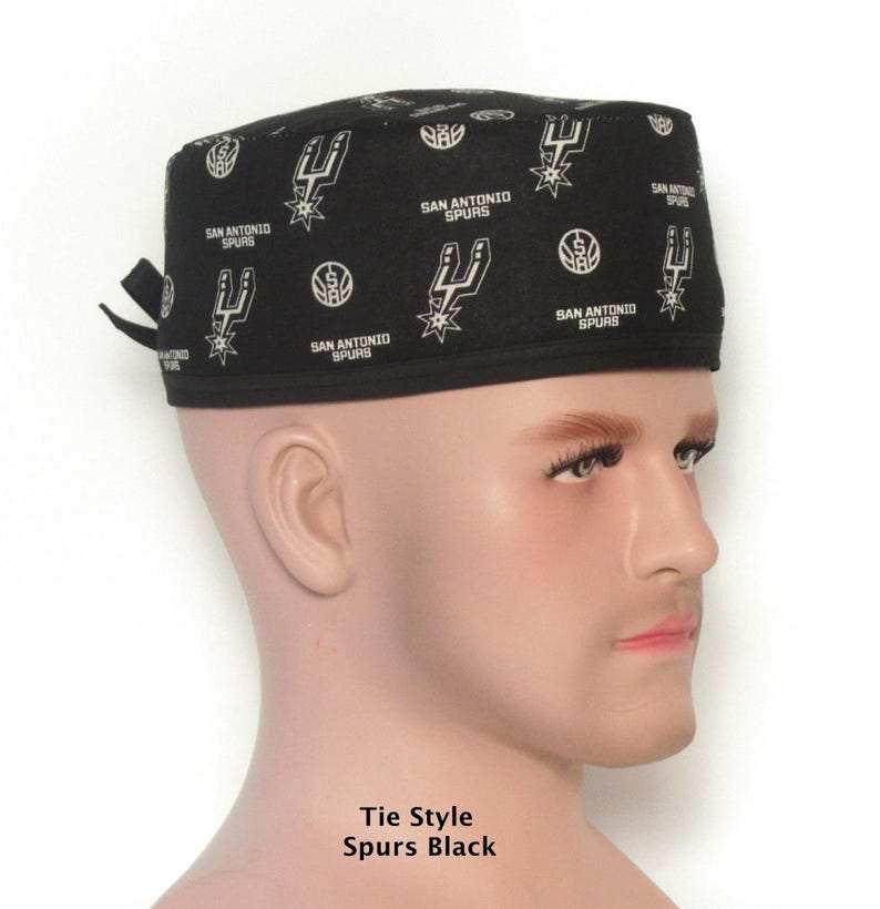 Puede incluir: Gorra negra estilo corbata con un patr&oacute;n blanco repetido del logotipo de los San Antonio Spurs. La gorra la lleva un maniqu&iacute;. El texto "SAN ANTONIO SPURS" tambi&eacute;n est&aacute; impreso en la gorra. El texto "Tie Style Spurs Black" est&aacute; impreso en la parte inferior.
