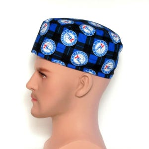 May include: A blue and black plaid cap featuring the Philadelphia 76ers logo. The cap has a repeating pattern of the team's logo in white and blue. The cap is worn by a mannequin.