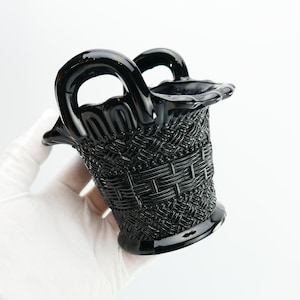 May include: A black glass basket with a woven pattern and two handles. The basket is made of dark glass and has a shiny finish.