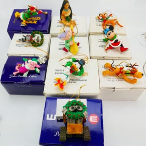 May include: A selection of Disney character Christmas ornaments, including Donald Duck, Mickey Mouse, and Pluto. Each ornament is in its original box. The boxes are white and blue.