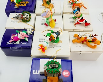 May include: A selection of Disney character Christmas ornaments, including Donald Duck, Mickey Mouse, and Pluto. Each ornament is in its original box. The boxes are white and blue.