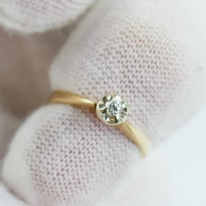 K&ouml;nnte beinhalten: Ein goldener Ring mit einem einzelnen runden Diamanten in einer Zargenfassung.