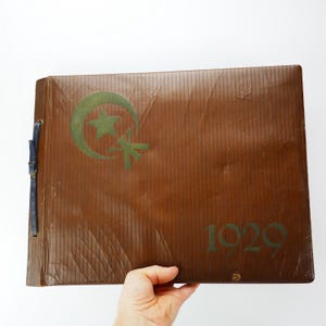 May include: A brown leather-bound photo album with a green crescent moon and star design. The year 1920 is printed on the front cover.