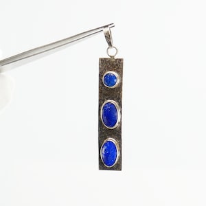 May include: A silver pendant featuring three oval-shaped lapis lazuli stones set in a vertical row. The pendant is on a silver chain.