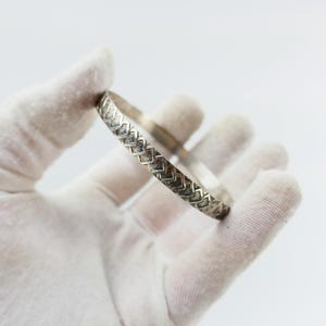 Può includere: Un braccialetto rigido in argento con un design testurizzato e intrecciato.