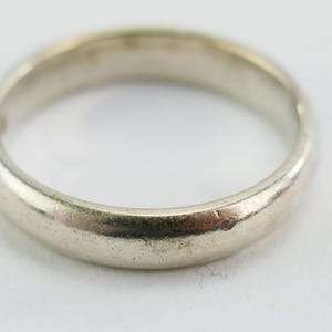 May include: A close-up of a silver ring with a slightly worn appearance. The ring has a smooth, rounded band and a subtle sheen, suggesting it may be made of a precious metal. The ring is a classic design, suitable for various occasions.
