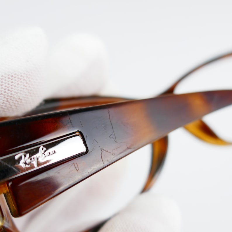 Peut inclure: Gros plan sur une monture en &eacute;caille de tortue brune avec un logo Ray-Ban argent&eacute;. La monture pr&eacute;sente quelques rayures &agrave; la surface.