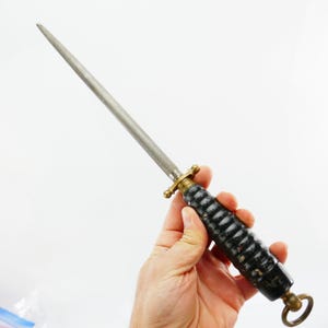 Op de afbeelding: Een stalen messenslijper met een zwart en gouden handvat. Het handvat heeft een textuur, geribbeld ontwerp. De slijper heeft een messing bescherming en een ring aan het einde van het handvat.