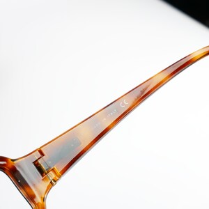 Peut inclure: Gros plan sur la monture en &eacute;caille brune d'une paire de lunettes. La monture porte l'inscription "MADE IN ITALY" et "CE" imprim&eacute;es &agrave; l'int&eacute;rieur.
