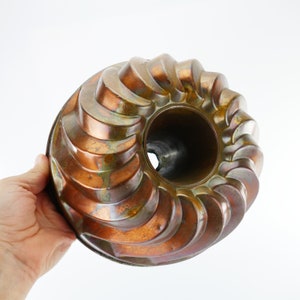 May include: A vintage copper-toned bundt cake pan with a fluted design. The pan has a worn, antique look with a greenish patina.