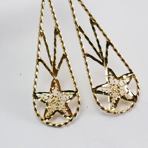 Puede incluir: Un par de pendientes de oro colgantes con un diseño en forma de estrella. Los pendientes están hechos de un delicado y complejo trabajo de alambre.