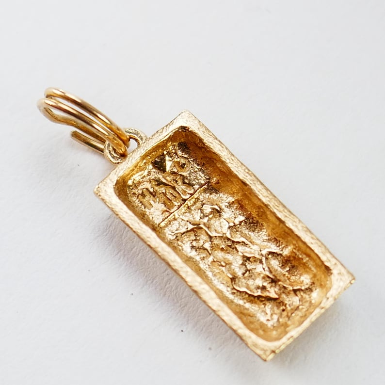 May include: Gold-colored metal keychain charm shaped like a rectangular bar with a textured surface. The charm has a ring attached to the top.