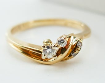 May include: A gold ring with a flowing design, featuring three small, clear gemstones. The ring has a polished finish and a delicate, elegant appearance, suitable for everyday wear or special occasions.