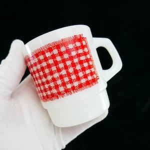 Puede incluir: Taza de cerámica blanca con un patrón de cuadros rojos y blancos. La taza tiene un asa y es perfecta para servir bebidas calientes.