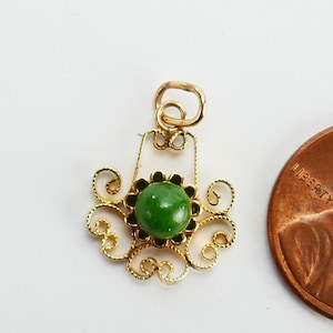 May include: A gold pendant featuring a green gemstone set in a filigree design. The pendant is approximately the size of a British penny.
