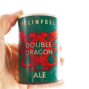 May include: A vintage green beer can with the text "FELINFOEL" at the top. The can features a red double dragon design with the words "DOUBLE DRAGON ALE". The can is held by a hand.
