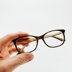 May include: Tortoise shell eyeglasses with gold metal accents. The glasses have a rectangular shape with rounded edges.
