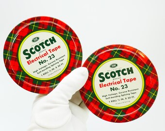 May include: Two red and green plaid round tins with white labels. The labels read "Scotch Electrical Tape No. 23 High Voltage, Corona Resistant Self-bonding Splicing Tape 1 Roll 3/4 in. x 30 ft. 19 mm x 91.4 cm."
