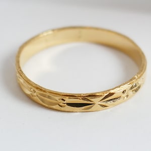 May include: A simple gold band ring with a decorative, engraved pattern.