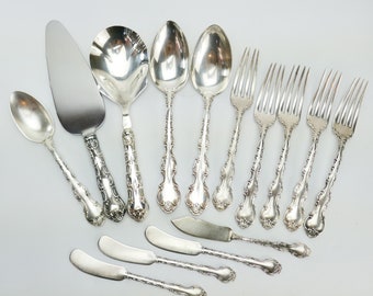 May include: A set of silverware, including a serving spoon, a cake server, a butter knife, and several forks and spoons. The silverware is made of silver and has an ornate design.